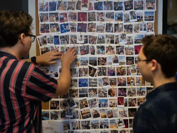 Twee mensen kijken naar een grote collage van meerdere foto's aan de muur.