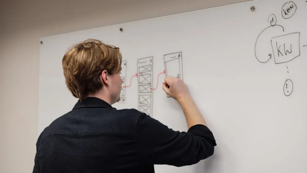 Iemand tekent diagrammen op een whiteboard met zwarte en rode markers.