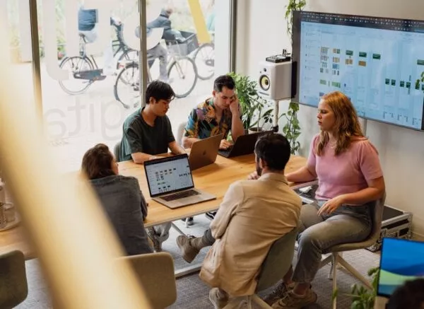 Een groep mensen werkt op laptops rond een tafel in een modern kantoor.