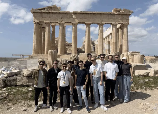 Een groep mensen, waaronder een back-endontwikkelaar, poseert bij de ruïnes van het Parthenon op een zonnige dag.